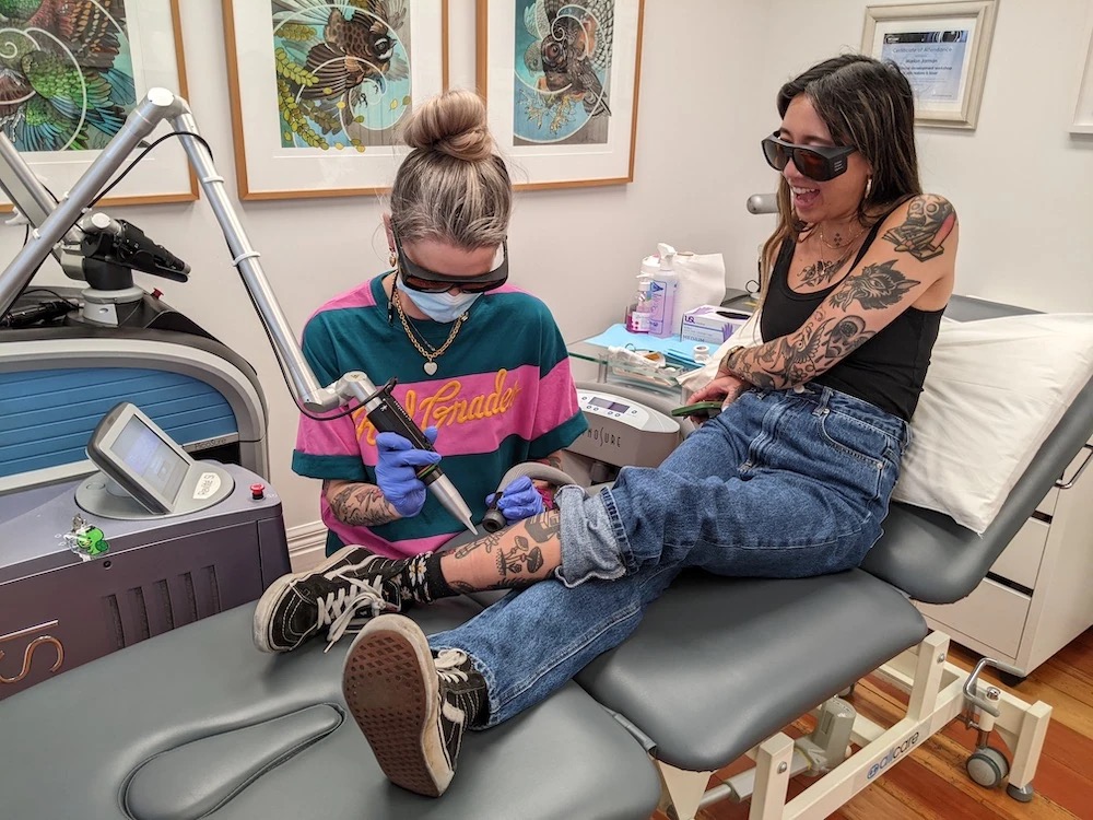 Tattoo artist performing laser tattoo removal on a client's leg at Sacred Laser.