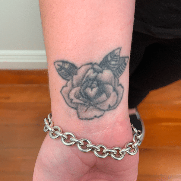 Person's wrist with a rose tattoo and silver chain bracelet